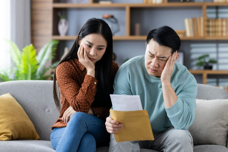Couple concerned with paperwork sitting on couch at home